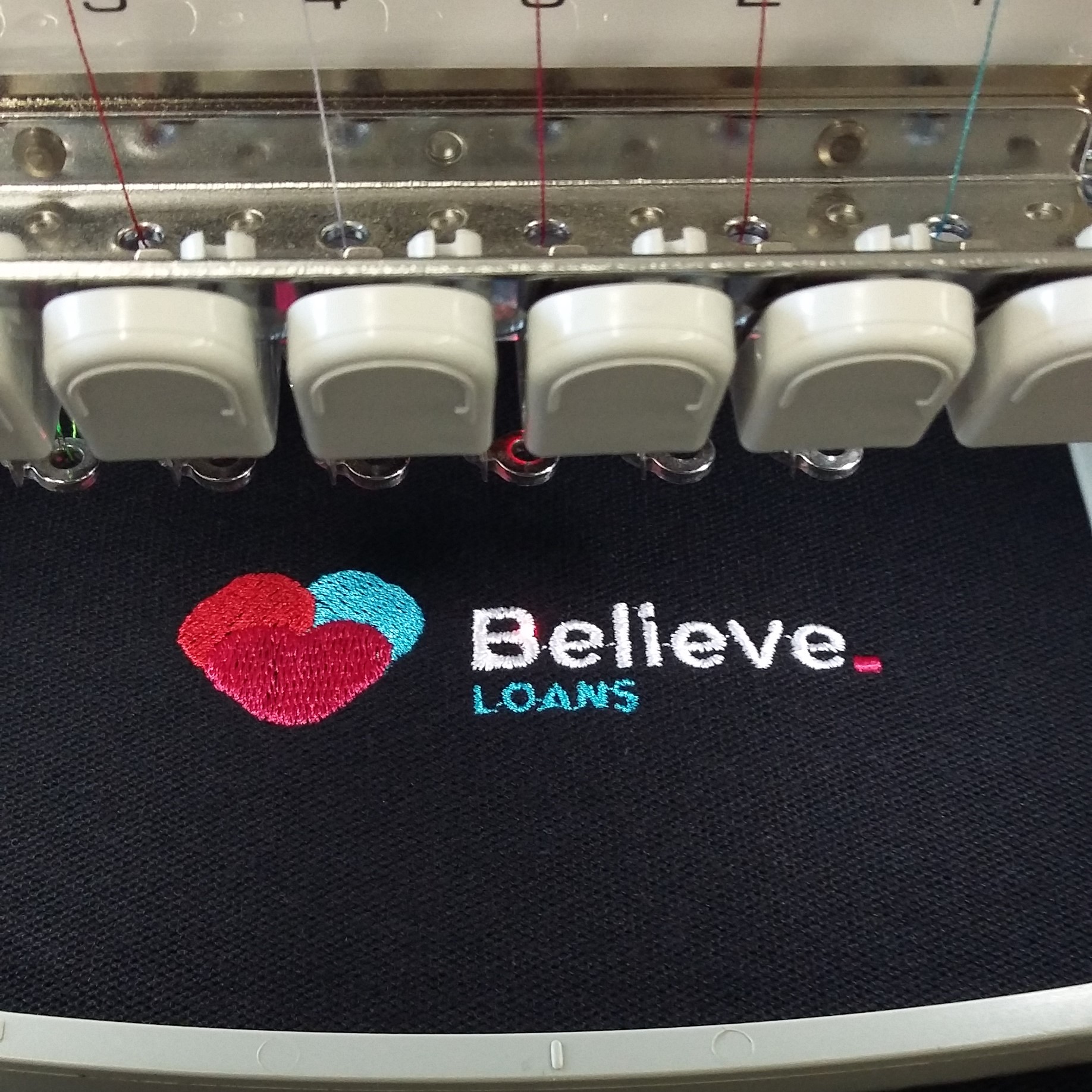 4 colour, Believe Loans logo 85mm across embroidered onto the chest of a black polo shirt.